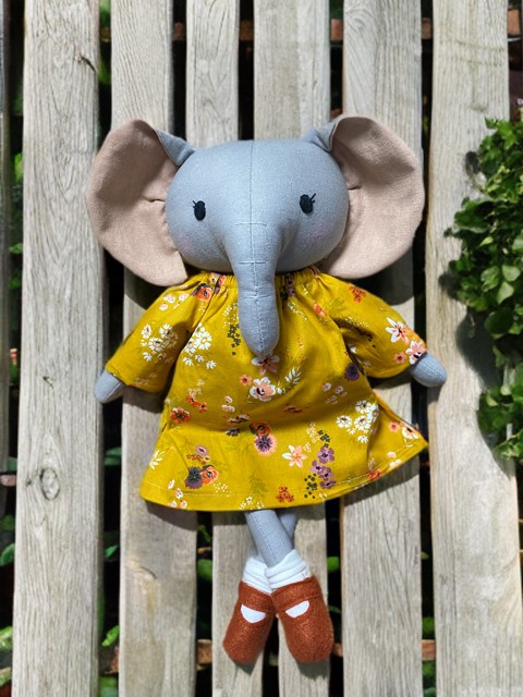 Elli Elefant mit einem gelben Blumenkleid, Socken und Schühchen. 