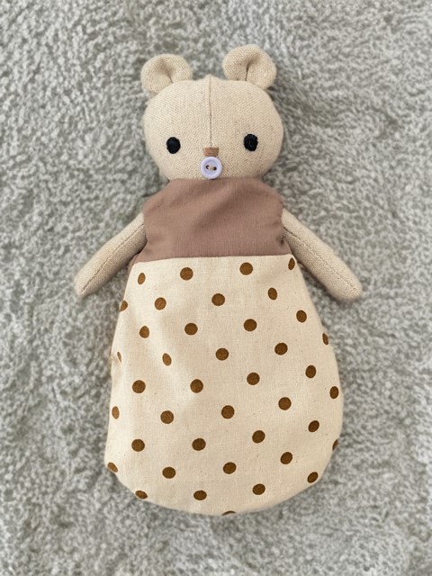 Kleiner Baby-Bär in einem gepunkteten braun- beigen Schlafsack liebvolles Spielzeuge für Kinder, ideal für Rollenspiele und Einschlafrituale. 