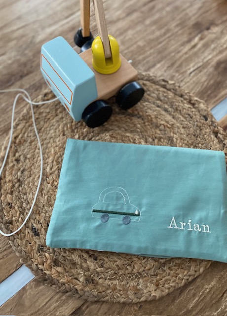 Türkise Wickeltasche mit Namenbestickung und kleinem Auto-Motiv, fotografiert mit Holzspielzeug.