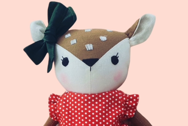 Nahaufnahme einer Stoffrehpuppe mit gestickten weissen Punkten, rosa Wangen und grosser dunkelgrüner Schleife am Ohr.