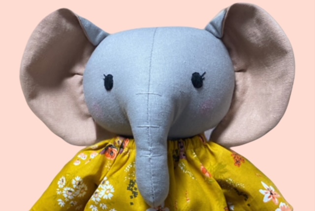 Nahaufnahme einer Stoff-Elefantenpuppe mit grossen Ohren, gesticktem Gesicht und gelben geblümten Kleid.