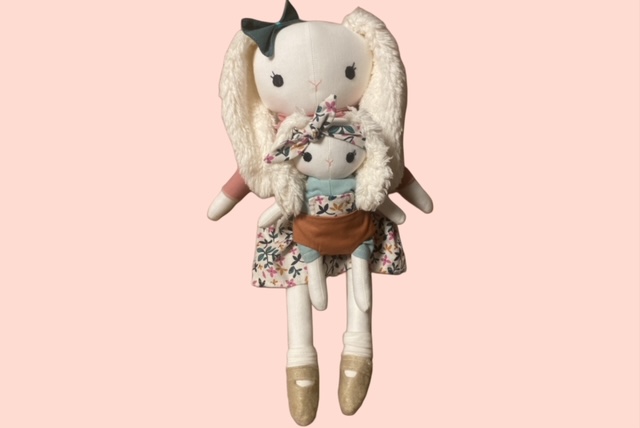 Grosse Stoff-Hasenpuppe mit flauschigen Ohren, floralem Kleid und Trage, in der eine kleinere Hasenpuppe sitzt.