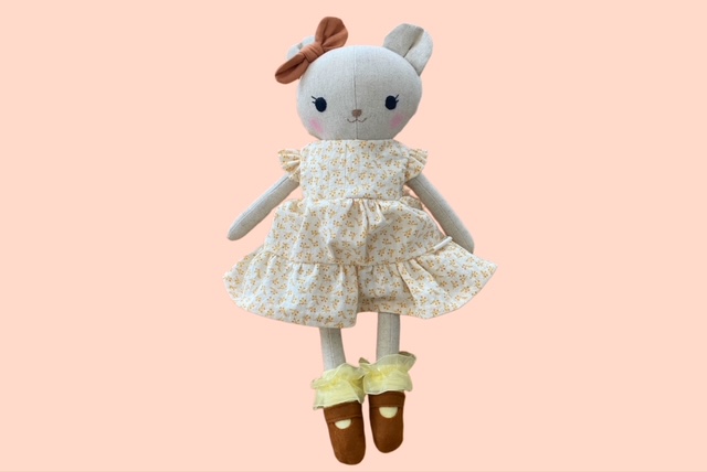 Stoff-Bärenpuppe mit braunfarbener Schleife, gelben Blumenkleid und braunen Schuhen mit gelben Rüschen 