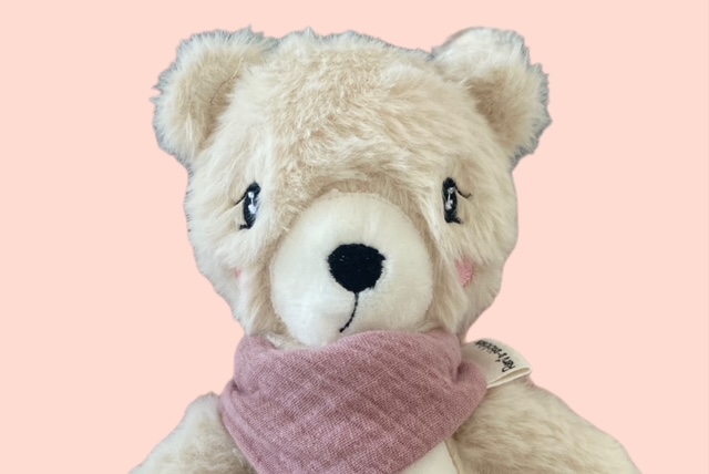 Nahaufnahme eines flauschigen cremefarbenen Stoffbären mit bestickten Gesicht und rosafarbenem Schal 