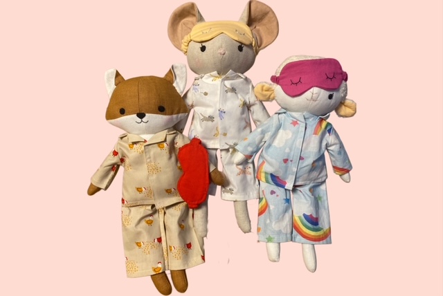 Drei handgemachte Stoffpuppen in liebevoll genähten Pyjamas, jeweils in unterschiedlichen Designs. Ein Fuchs- Puppe, eine Maus-Puppe und eine Schaf-Puppe tragen Schlafanzüge mit verspielten Mustern und stehen nebeneinander auf hellem Hintergrund.

