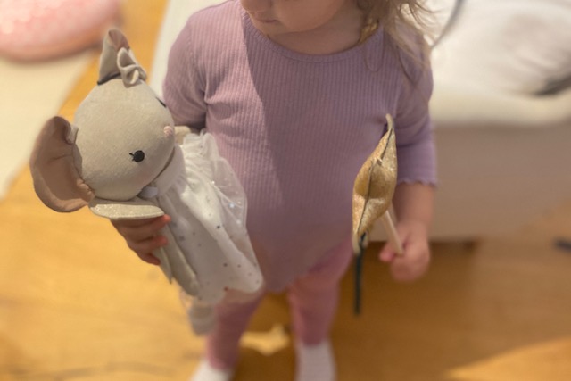 Ein Kind hält eine handgemachte Stoffpuppe mit glitzerndem Sternoutfit in der Hand. Die Szene spielt im Kindezimmer. 