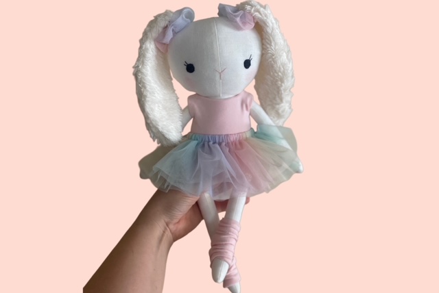 Hand hält eine handgemachte Stoffpuppe im Ballerina-Outfit mit pastellfarbenem Tüllrock und langen flauschigen Ohren.