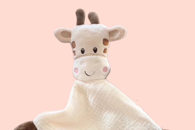 Nahaufnahme des Schmusetuchs Giraffe vor rosa Hintergrund.