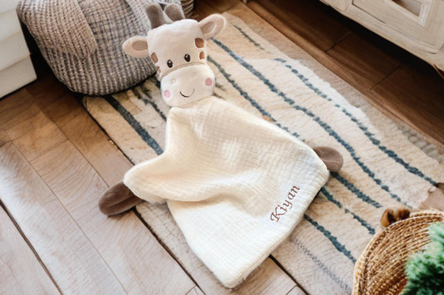 Schmusetuch Giraffe mit bestickten Namen auf einem gemütlichen Kinderzimmerteppich arrangiert.