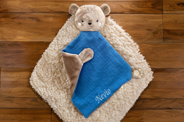Personalisierbares Schmusetuch Bär in Blau mit Namen, liebevoll auf einem weichen Teppich im Kinderzimmer präsentiert. 