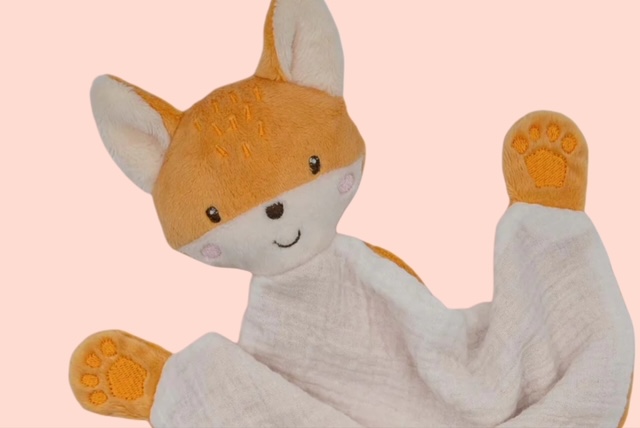 Nahaufnahme des Schmusetuchs Fuchs mit freundlichen Plüschgesicht und bestickten Details auf rosa Hintergrund.