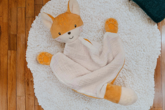 Schmusetuch Fuchs auf einem runden, flauschigen Teppich in einer warmen Kinderzimmer- Umgebung.