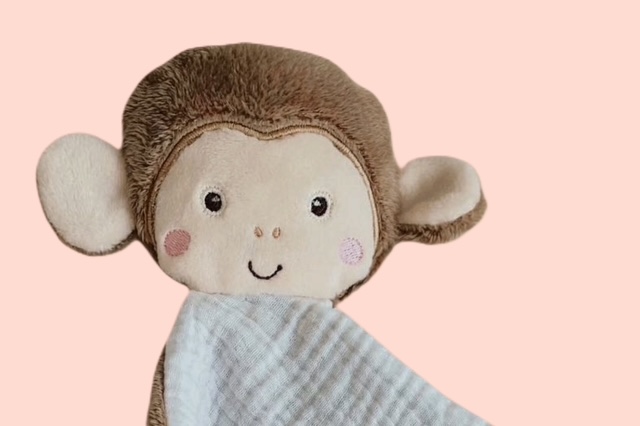 Nahaufnahme des Schmusetuchs Affe mit süssen Gesicht und weissem Musselinstoff auf rosa Hintergrund.