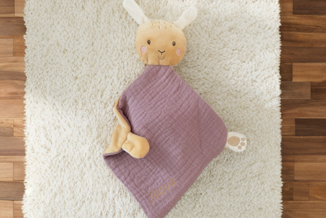 Personalisierbares Schmusetuch Hase in Altrosa, liebevoll auf einem cremefarbenen Teppich im Kinderzimmer arrangiert. 