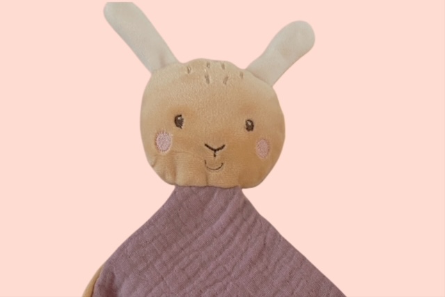 Nahaufnahme des Hasen-Kuscheltuchs mit weichem beige-farbenem Kopf rosa Wangen auf rosa Hintergrund.