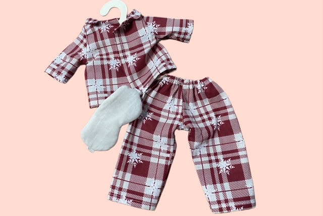 Puppen- Pyjamaset im rot-beigen Karomuster mit Oberteil, Hosen und Schlafmaske auf rosa Hintergrund.