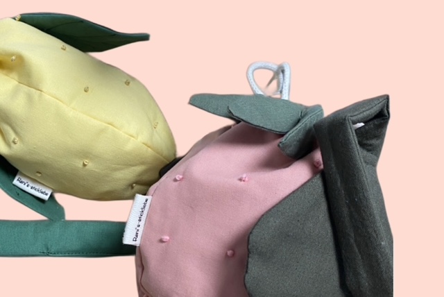 Nahaufnahmen von zwei handgemachten Stoff-Taschen in Erdbeer-Zitronenform, mit zarten Stickdetails und grünen Blätter als Verzierung.