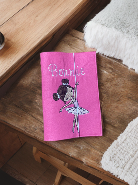Personalisierte Gesundheitshefthülle aus Filz in Pink mit Ballerina-Motiv, liegend auf der Wickelkommode. 