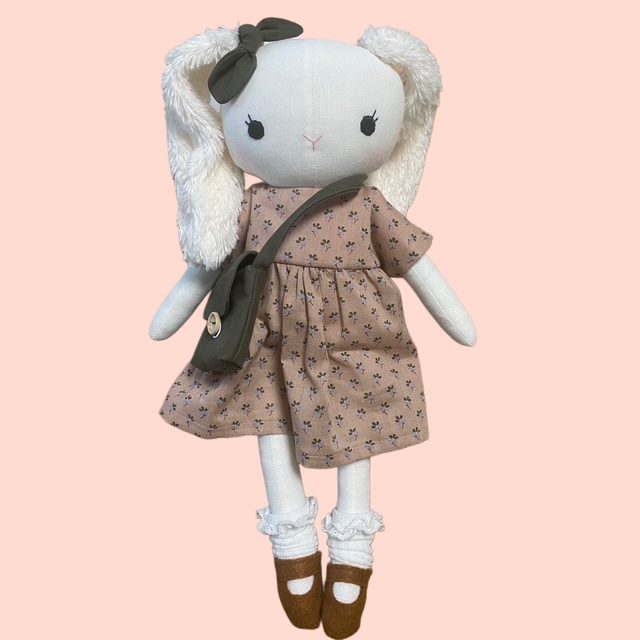 Handgemachte Stoffpuppe Hase mit Kleid und Umhängetasche Kuschelpuppe für Kinder auf rosa Hintergrund.
