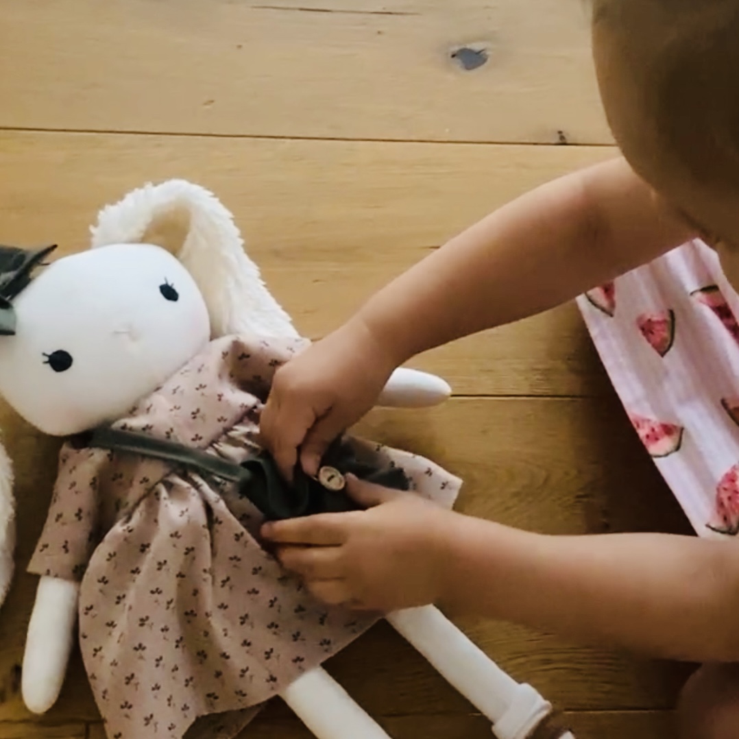 Stoffpuppe Hase wird von Kinderhänden angezogen, weich handgemachte Puppe zum Spielen und Anziehen.