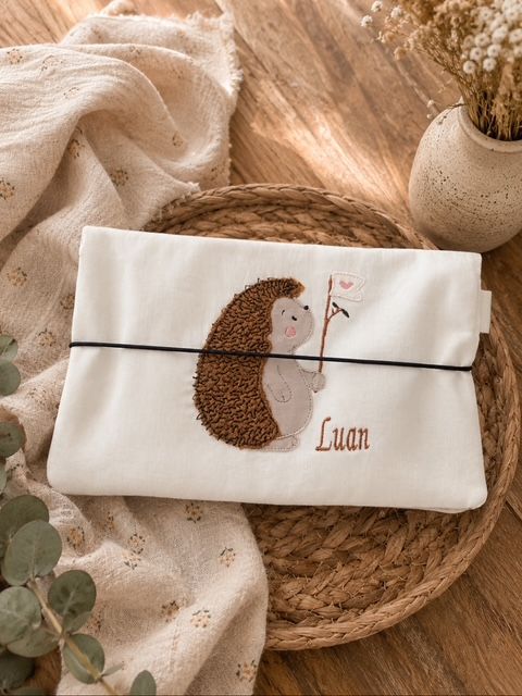 Handgemachte Wickeltasche mit Igel-Motiv auf einem dekorativen Holztisch. 