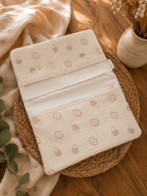 Offene Wickeltasche mit einem Igel-Motiv Stoff in beige. mehreren Fächern für Windel, Feuchtetücher und Babyzubehör. Auf einem Holztisch präsentiert.  

