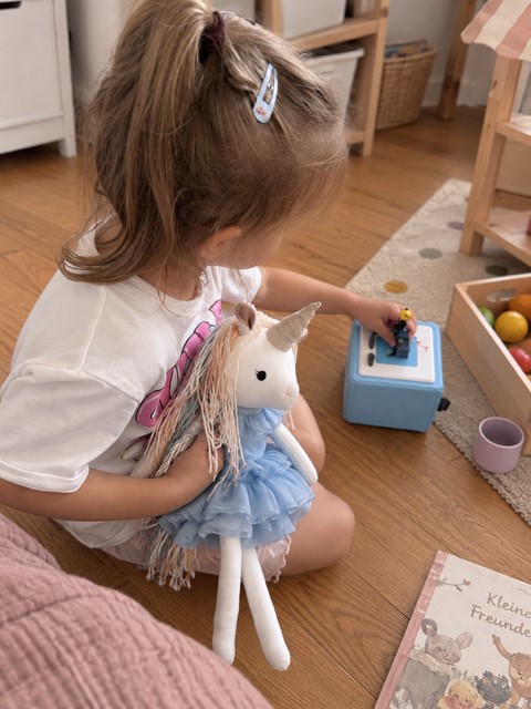Kind spielt im Kinderzimmer mit dem handgemachten Einhorn Lilliana im hellblauen Prinzessinnenkleid.