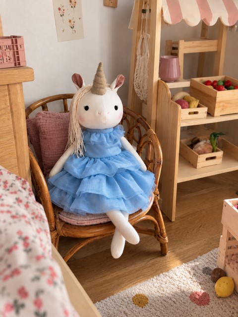 Handgemachtes Einhorn Lilliana mit hellblauen Kleid in einer gemütlichen Kinderzimmer- Spielecke.